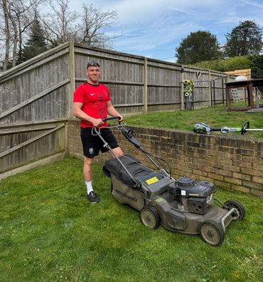 Man in red shirt mowing the lawn with a lawnmower.