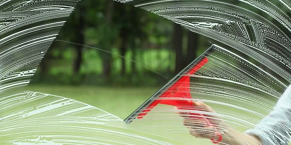 A person cleaning a window with a red squeegee outdoors.