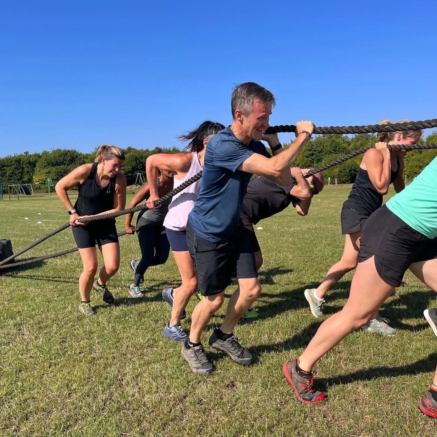 A group pulls a heavy rope together in a sunny outdoor exercise.