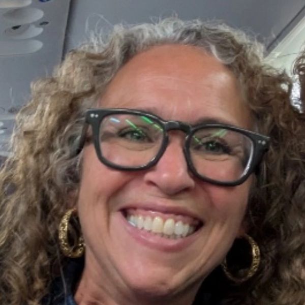 Smiling woman with curly hair and large glasses.