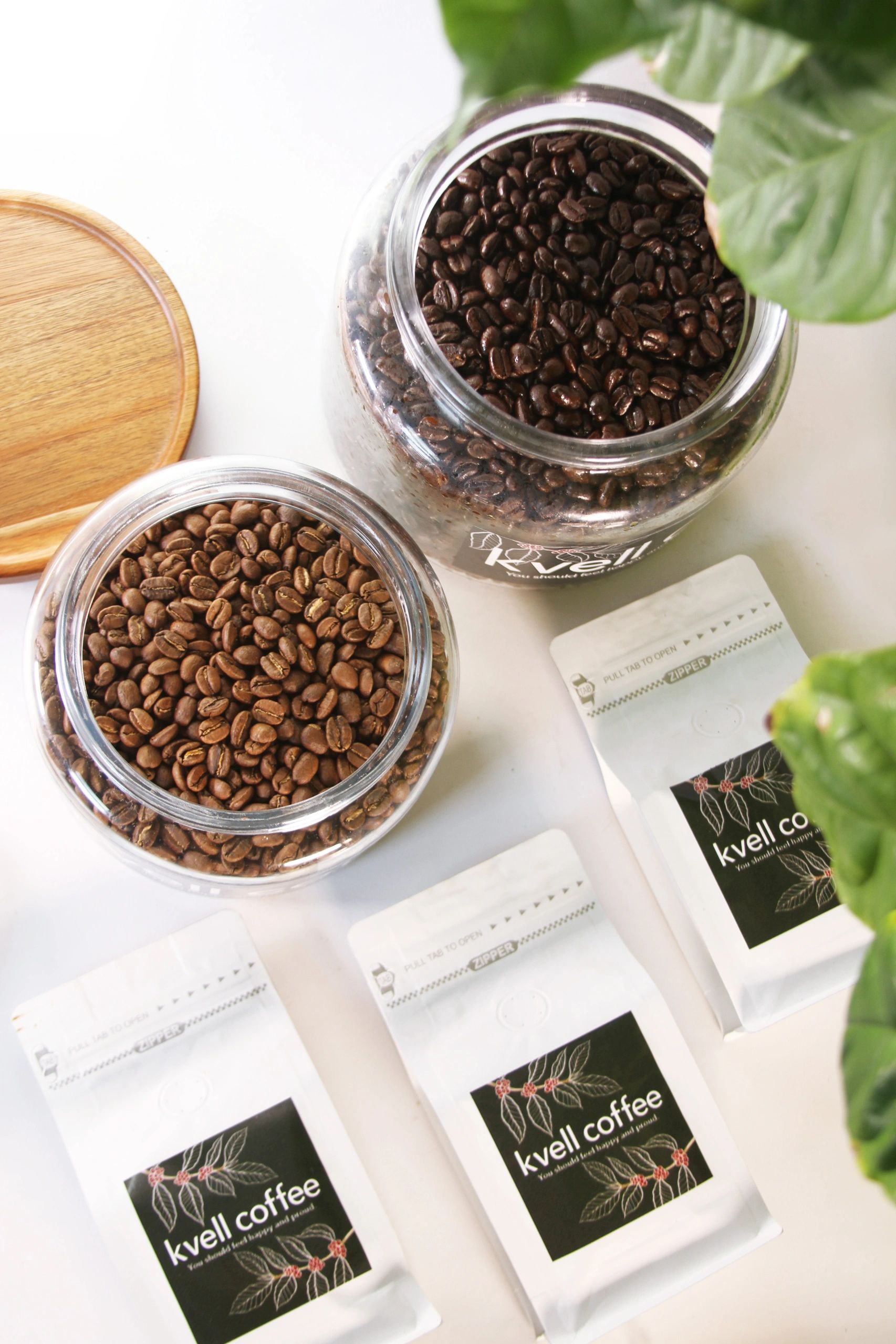 Two jars of coffee beans and several bags of Kvell Coffee on a white surface.
