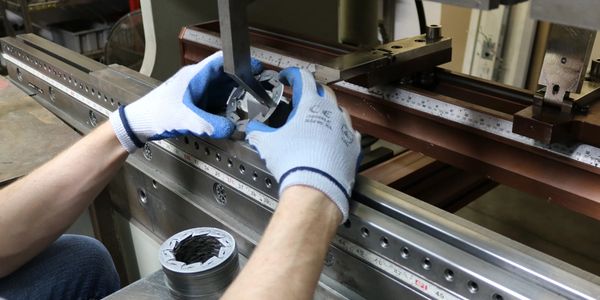 A person holding a circular part and bending the metal using a press brake. 