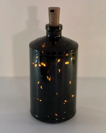 Dark bottle with tiny glowing lights inside and a cork stopper on top.