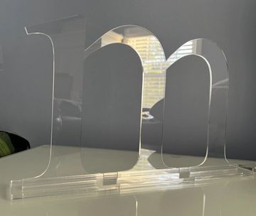 Clear acrylic sculpture shaped as "1m" on a white surface.