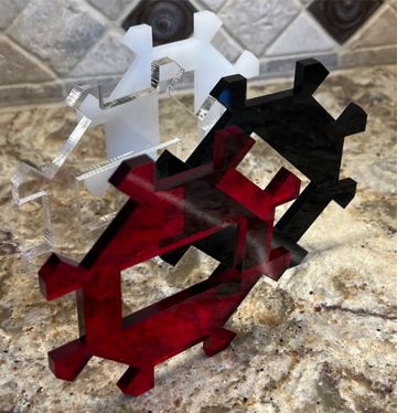 Three interlocking gear-shaped acrylic pieces in white, black, and red on a granite surface.
