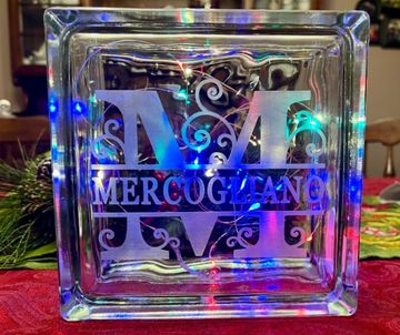 Decorative glass block with "M Mercogliano" etched, illuminated by colorful lights.