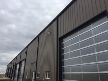 Exterior view of a large industrial building with multiple garage doors under a cloudy sky.