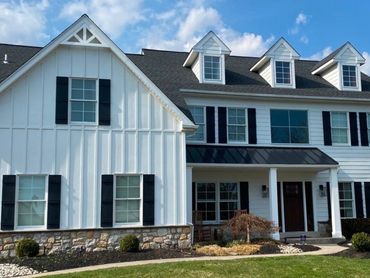 Modern two-story white house with black shutters and stone foundation under a blue sky.