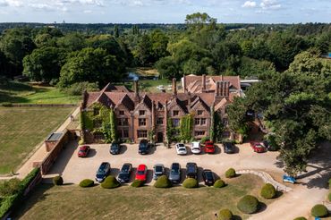 A large historic mansion surrounded by greenery with cars parked in front.