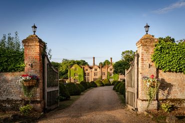 Elegant historic mansion with open gates and manicured gardens under clear blue sky.