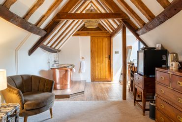 Cozy attic room with wooden beams, a copper bathtub, and vintage furniture.