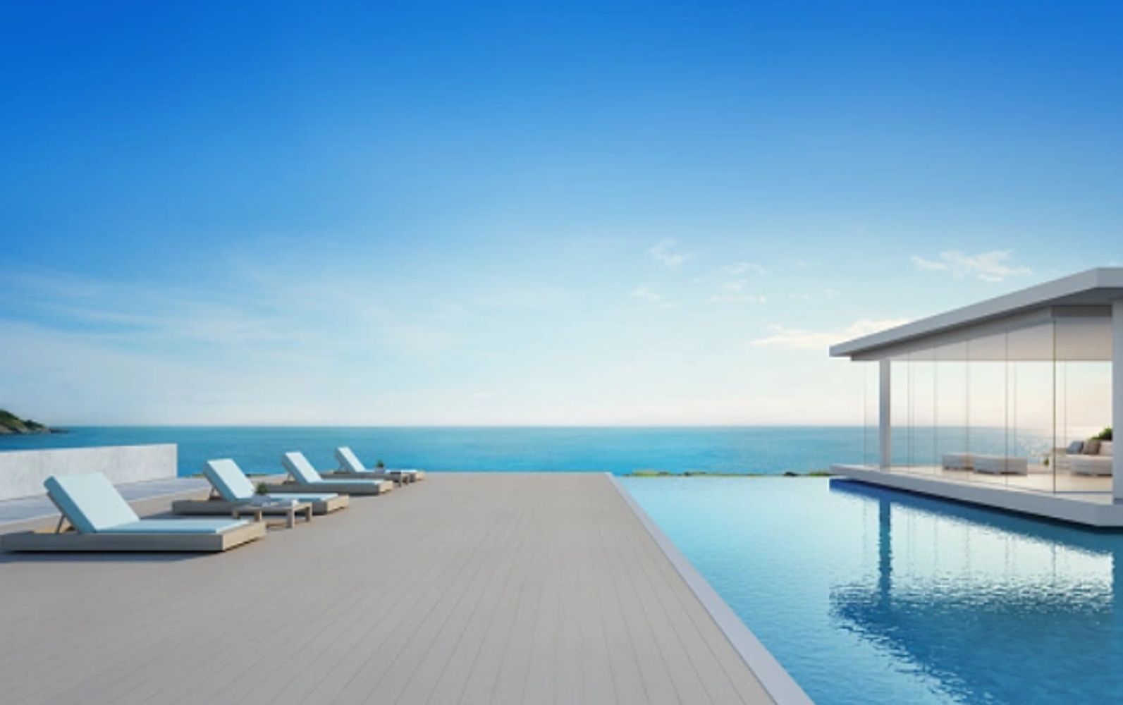 Serene pool deck scene showing deck, glass front adjacent building, lounge chairs, and ocean beyond.
