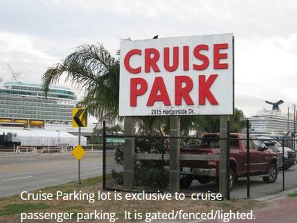 Cruise park sign near a cruise ship dock with parked vehicles.