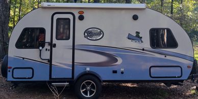 Compact white and blue camper trailer parked outdoors among trees.
