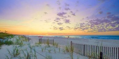 Serene beach at sunset with sand dunes and wooden fences.