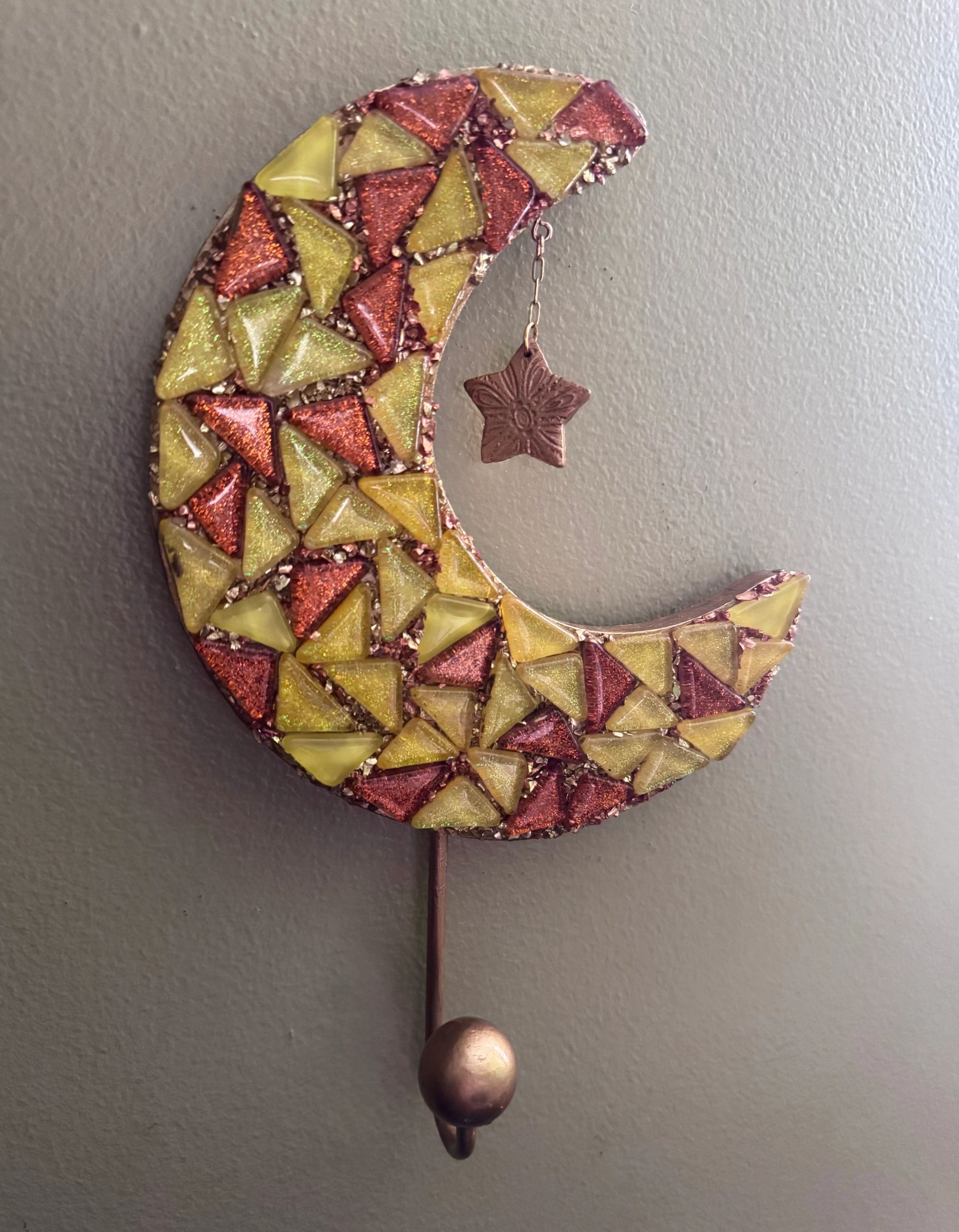 Decorative crescent moon with red and yellow triangular pieces and a hanging star charm.