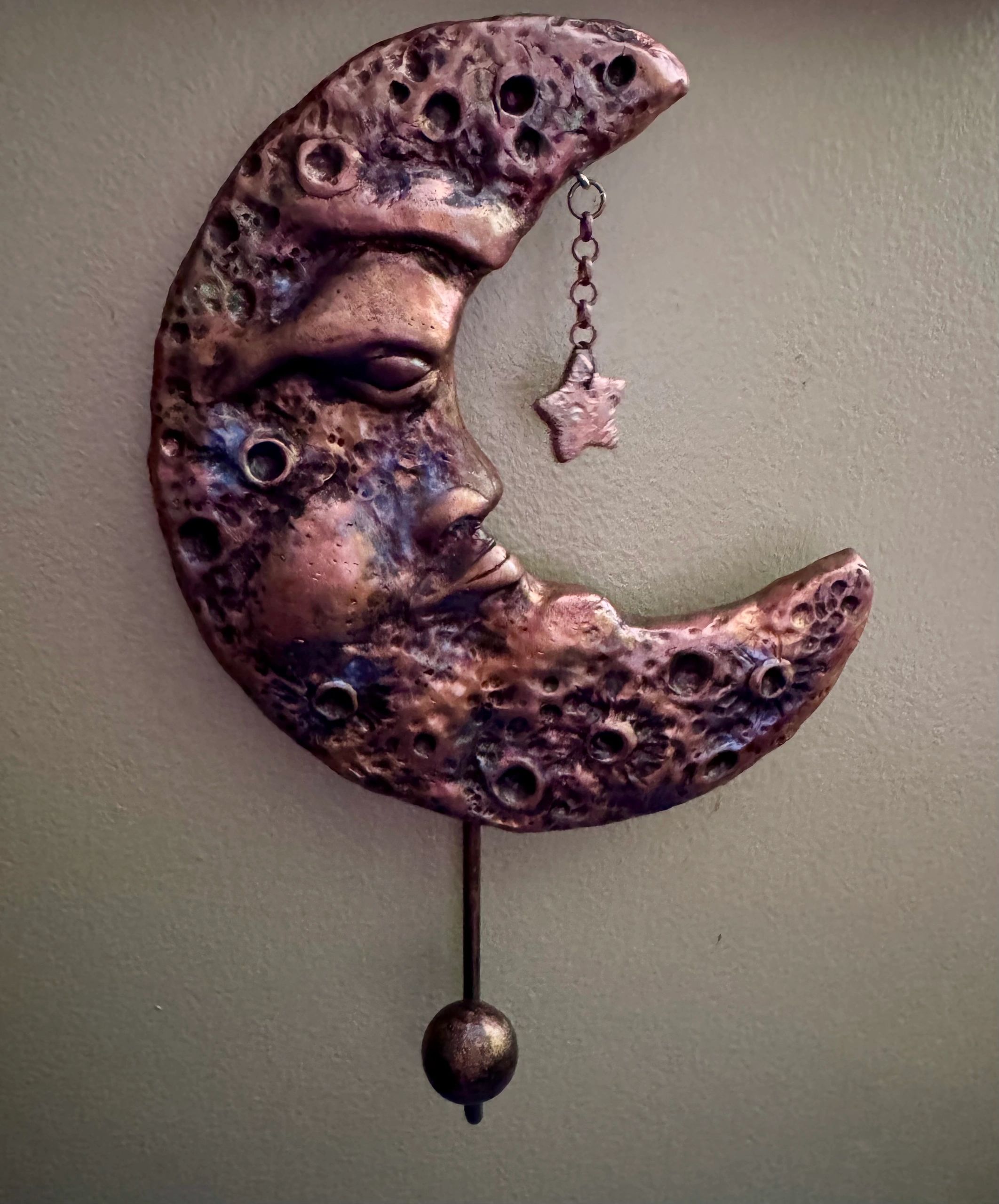 Decorative crescent moon sculpture with a hanging star and textured surface.