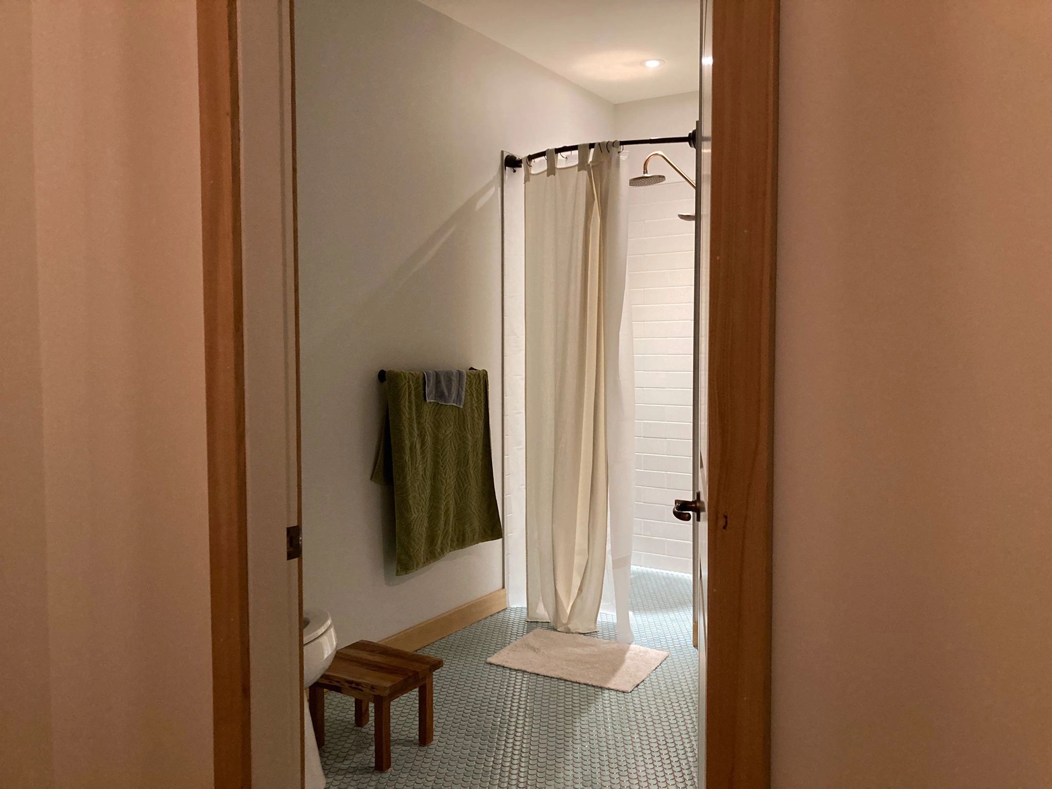 Minimalist bathroom with green towel and cream shower curtain.