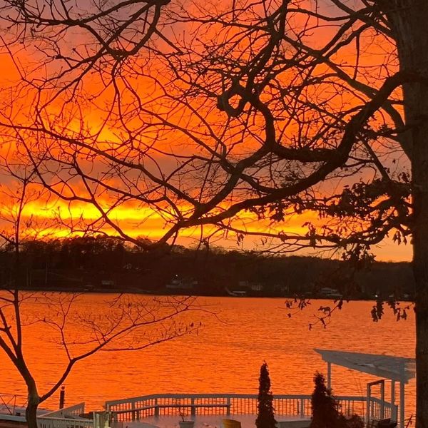 Fiery orange sunset over a lake with silhouetted trees.