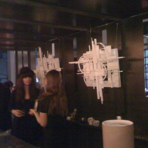Two women talk near abstract wall art in a dimly lit room.