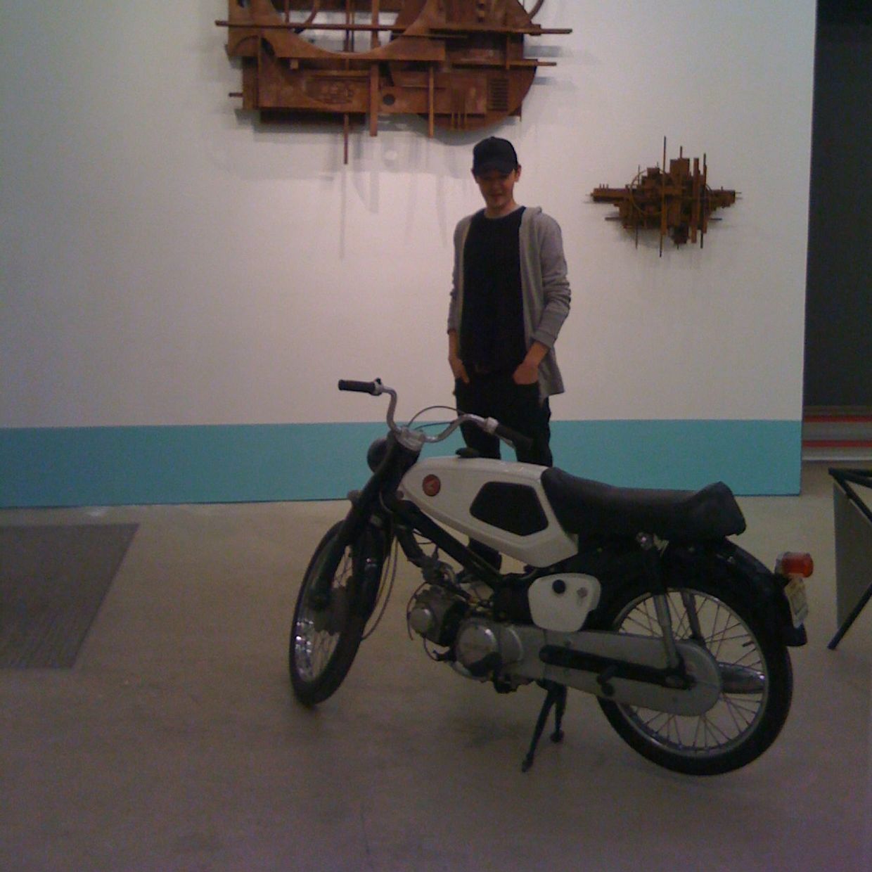 Person standing next to a vintage motorcycle in an art gallery.