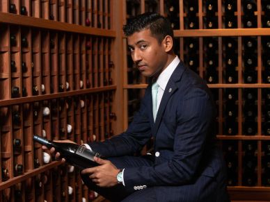 A man in a suit selecting a wine bottle in a cellar.