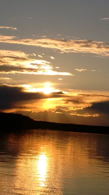 Golden sunset reflecting on calm lake waters with silhouetted horizon.