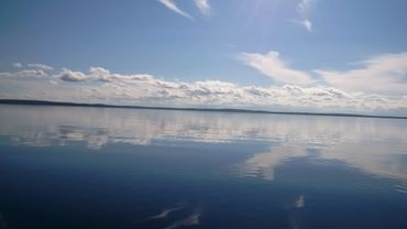 Calm lake with blue sky and scattered clouds reflected on water.