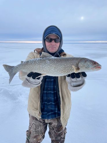 Man holding a large fish on a snowy frozen lake.