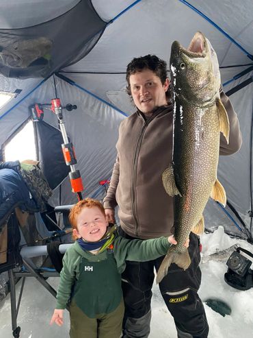 A man and child proudly display a large fish inside an ice fishing tent.