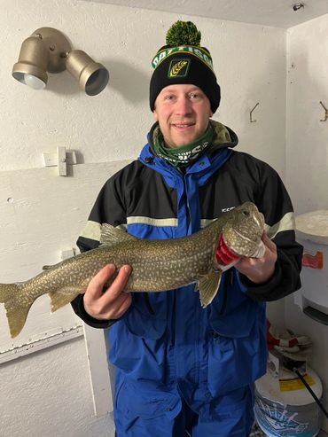 Man in winter gear holding a large fish indoors.