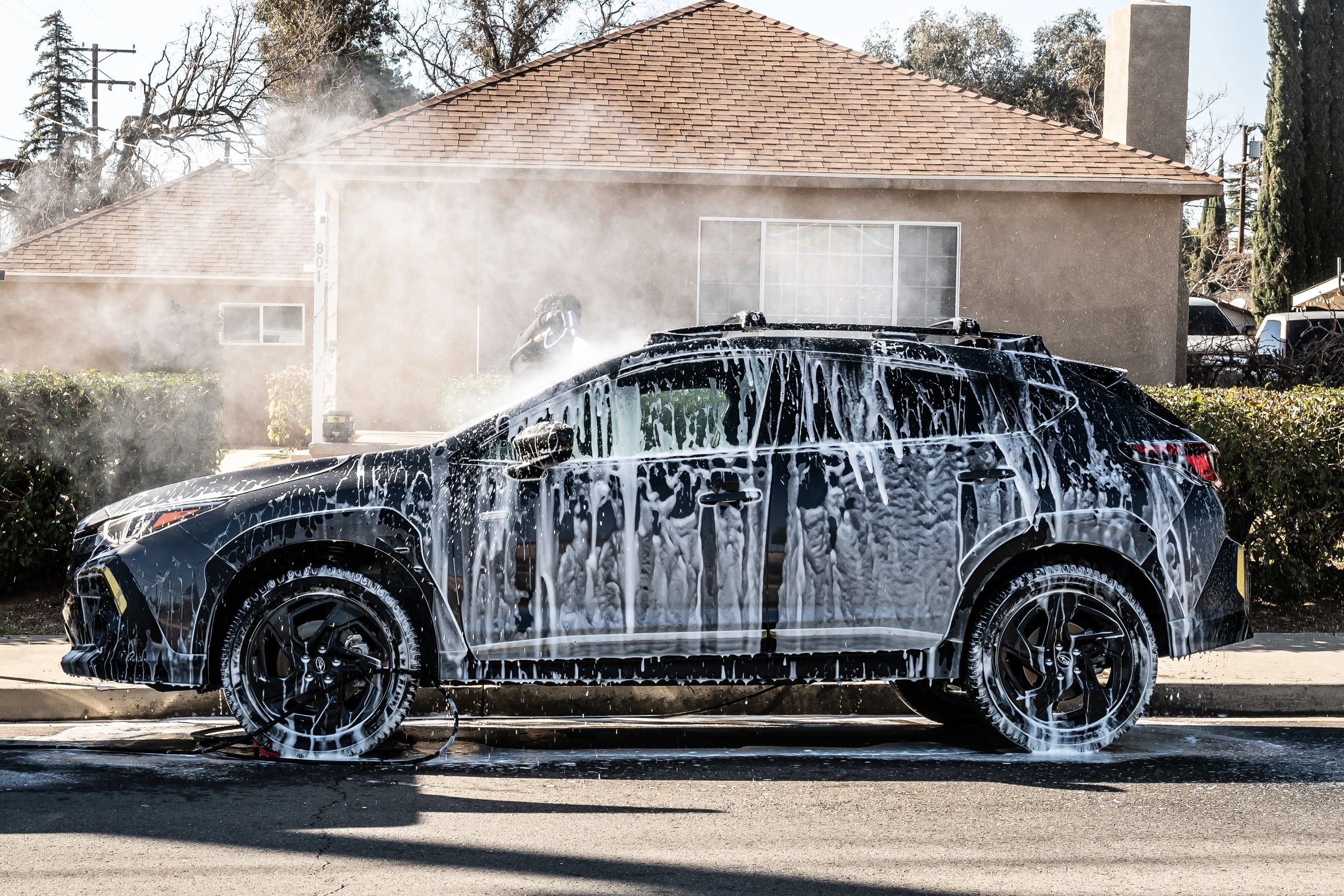 Black car covered in soap suds being washed.