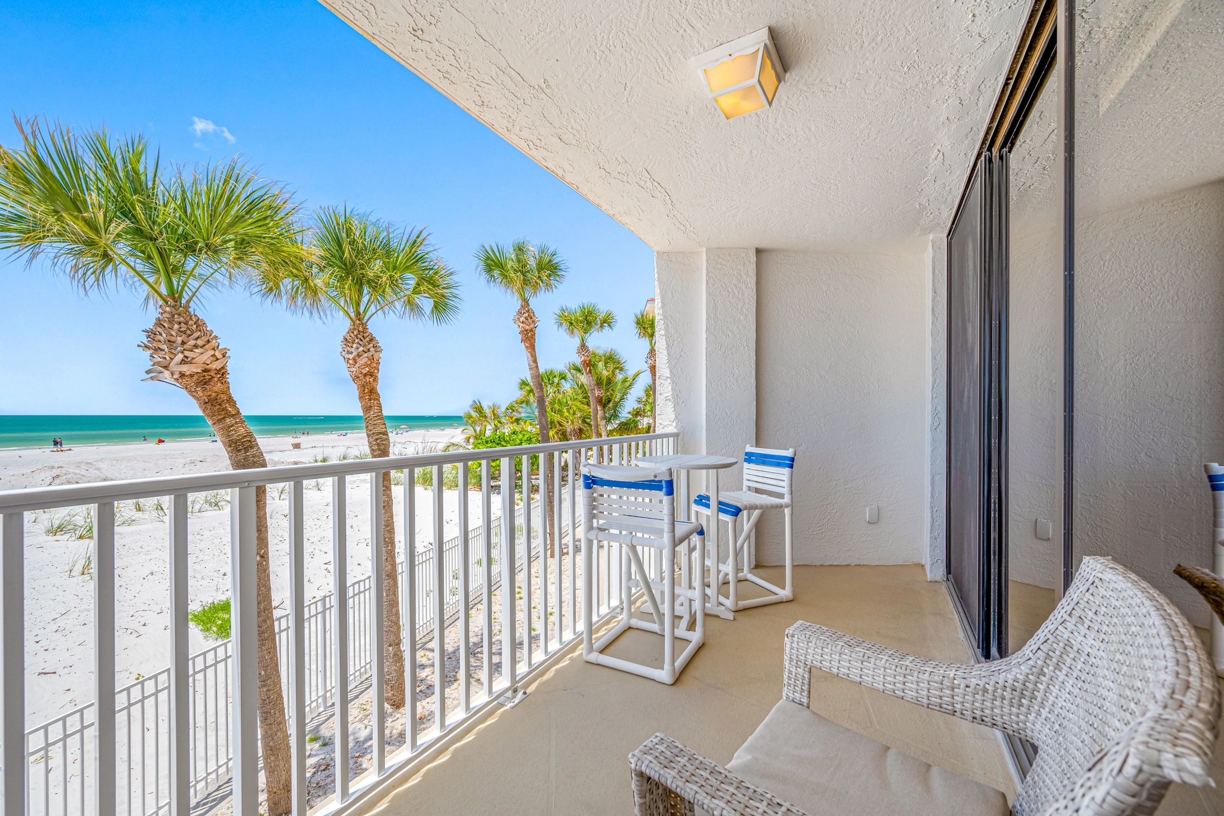 Beachfront balcony with white furniture and palm tree views.