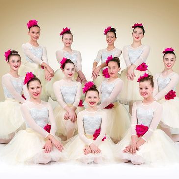 Group of ballerinas in white tutus with pink flowers.