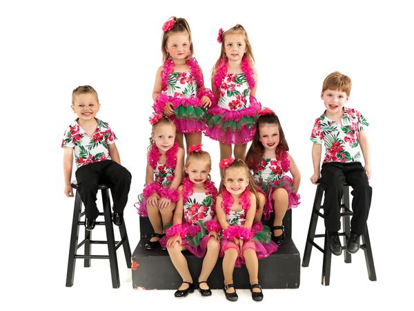 Group of kids wearing pink flowery costumes. Two boys are on stools and the six girls are on stairs.