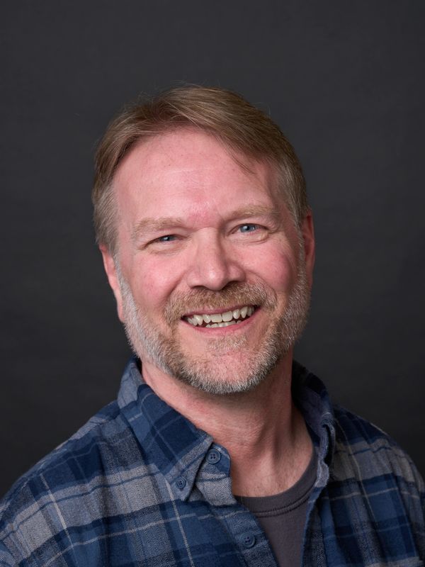 Smiling middle-aged man with a beard in a blue plaid shirt.