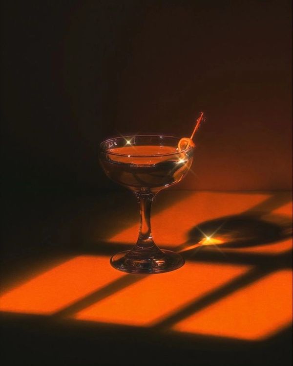 A cocktail glass with an olive, glowing under warm orange light.