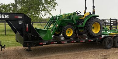 Green John Deere tractor on a black Tiger trailer in a rural area.