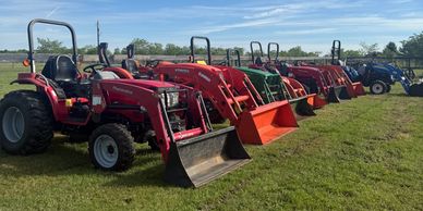 Row of colorful tractors lined up on a grassy field under a blue sky.
