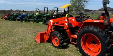 A row of colorful tractors lined up on grass under a clear sky.
