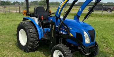 Blue New Holland tractor parked on green grass under clear sky.