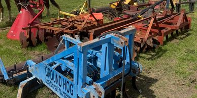 Various farm equipment arranged on grass with a horse behind a fence.