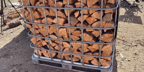 Stacked firewood neatly packed in a metal cage outdoors.