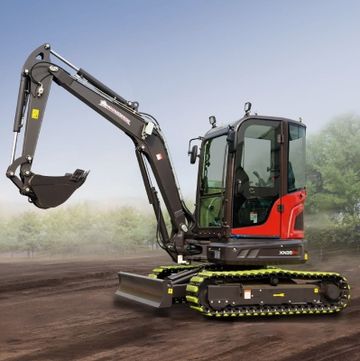 Compact excavator with bright yellow tracks on dirt ground against a clear sky.