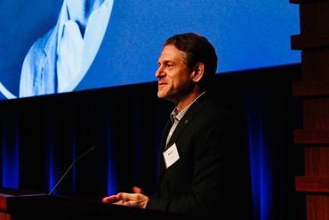 Man speaking at a podium with a blue backdrop.