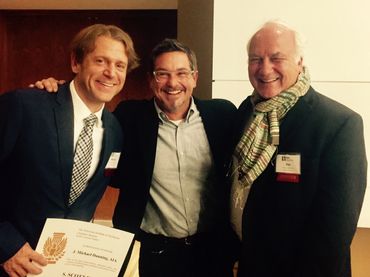 Three men smiling, one holding a certificate.