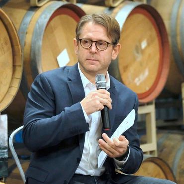 Man speaking with microphone in front of barrels.