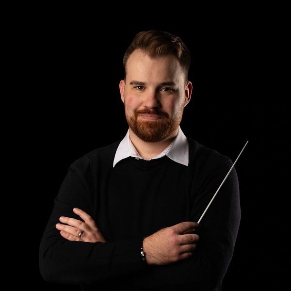 Man with a beard holding a conductor's baton.