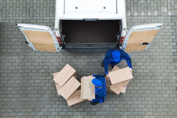 Two delivery workers, who appear to be men, loading cardboard boxes into the back of a white van.