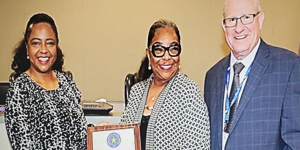 Three people posing, middle holding a plaque.